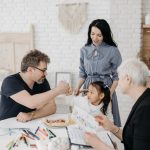 Criança conversa com adultos responsáveis e uma profissional de assistência social em uma sala de casa.