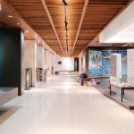 Corredor amplo e iluminado de uma exposição de design contemporâneo, com obras dispostas ao longo do espaço.