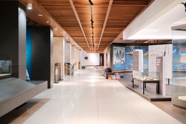 Corredor amplo e iluminado de uma exposição de design contemporâneo, com obras dispostas ao longo do espaço.